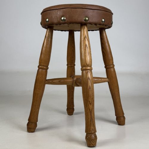 fig 2. A circular antique oak stool featuring a padded brown leather seat secured with brass studs, supported by four turned legs and cross stretchers.