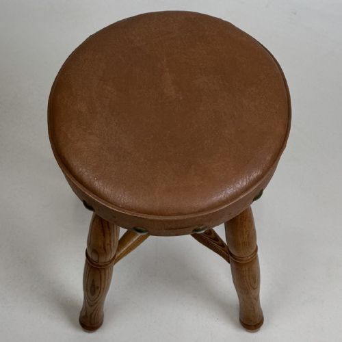 fig 8. A circular antique oak stool featuring a padded brown leather seat secured with brass studs, supported by four turned legs and cross stretchers.