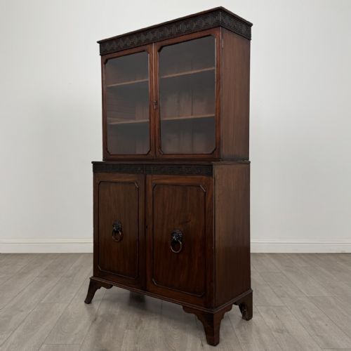 fig 1. An eighteenth-century Georgian mahogany glazed bookcase featuring an upper cabinet with glass doors and a lower cabinet with carved doors, lion mask handles, and Greek key frieze details.