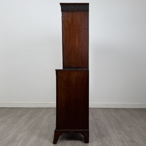 fig 2. An eighteenth-century Georgian mahogany glazed bookcase featuring an upper cabinet with glass doors and a lower cabinet with carved doors, lion mask handles, and Greek key frieze details.