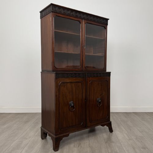 fig 7. An eighteenth-century Georgian mahogany glazed bookcase featuring an upper cabinet with glass doors and a lower cabinet with carved doors, lion mask handles, and Greek key frieze details.