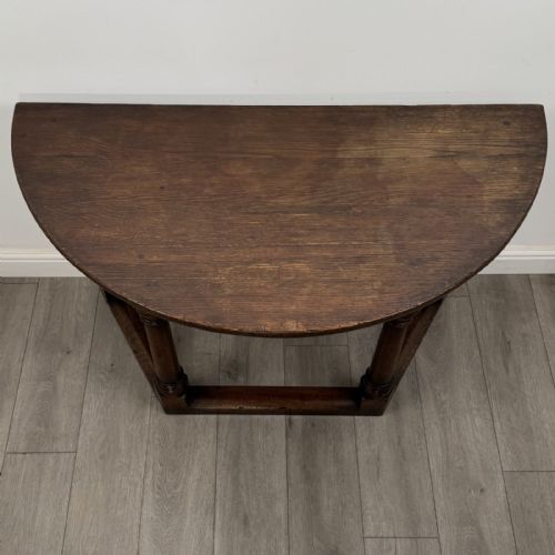 fig 6. A dark oak demi-lune side table featuring turned legs and a low perimeter stretcher base.