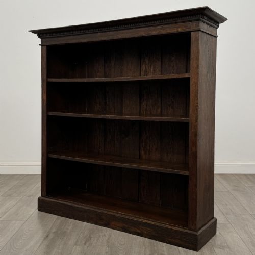 fig 1. An antique dark oak open bookcase featuring four shelf sections, a dentil carved cornice at the top, and a solid base.
