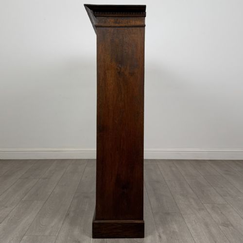 fig 2. An antique dark oak open bookcase featuring four shelf sections, a dentil carved cornice at the top, and a solid base.