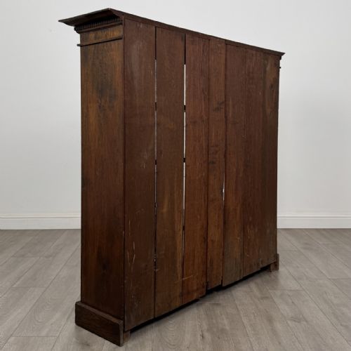 fig 3. An antique dark oak open bookcase featuring four shelf sections, a dentil carved cornice at the top, and a solid base.