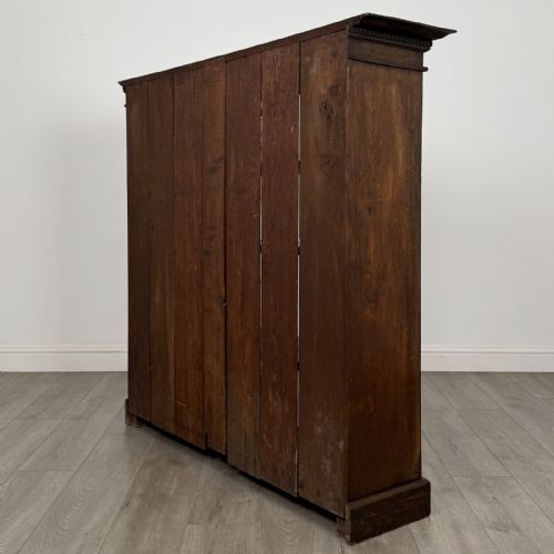 fig 5. An antique dark oak open bookcase featuring four shelf sections, a dentil carved cornice at the top, and a solid base.