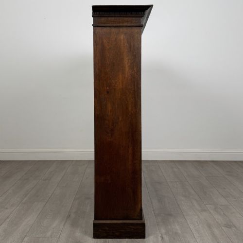 fig 6. An antique dark oak open bookcase featuring four shelf sections, a dentil carved cornice at the top, and a solid base.