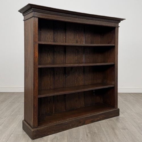 fig 7. An antique dark oak open bookcase featuring four shelf sections, a dentil carved cornice at the top, and a solid base.