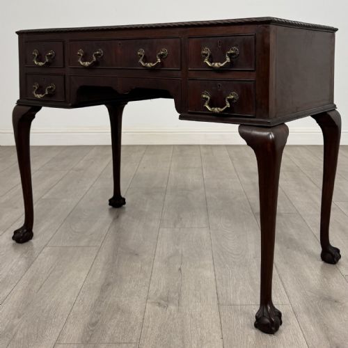 fig 1. An Edwardian dark mahogany writing table with five drawers, decorative brass handles, a carved top edge, and cabriole legs ending in ball and claw feet.