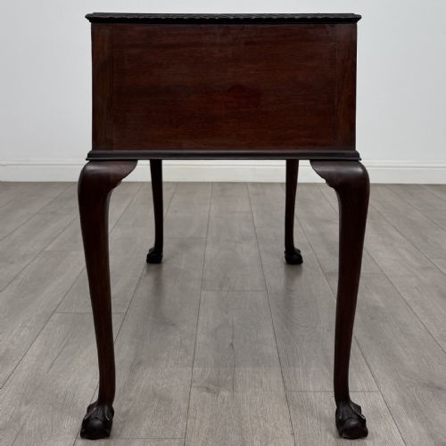 fig 2. An Edwardian dark mahogany writing table with five drawers, decorative brass handles, a carved top edge, and cabriole legs ending in ball and claw feet.