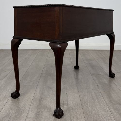 fig 3. An Edwardian dark mahogany writing table with five drawers, decorative brass handles, a carved top edge, and cabriole legs ending in ball and claw feet.