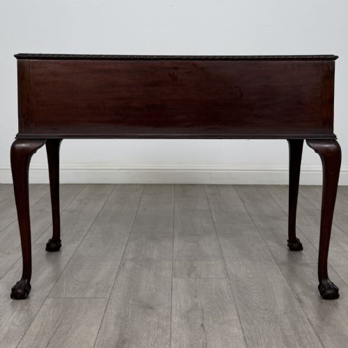 fig 4. An Edwardian dark mahogany writing table with five drawers, decorative brass handles, a carved top edge, and cabriole legs ending in ball and claw feet.
