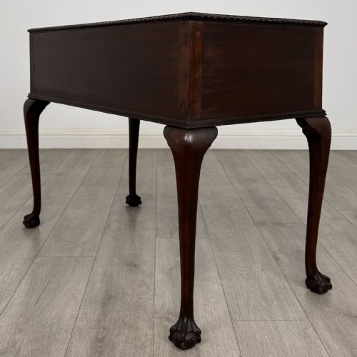 fig 5. An Edwardian dark mahogany writing table with five drawers, decorative brass handles, a carved top edge, and cabriole legs ending in ball and claw feet.