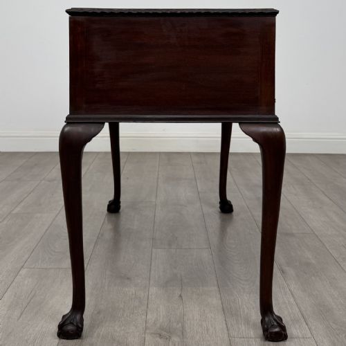 fig 6. An Edwardian dark mahogany writing table with five drawers, decorative brass handles, a carved top edge, and cabriole legs ending in ball and claw feet.