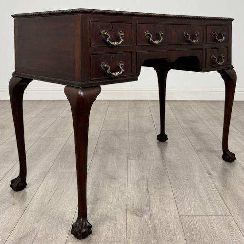 fig 7. An Edwardian dark mahogany writing table with five drawers, decorative brass handles, a carved top edge, and cabriole legs ending in ball and claw feet.