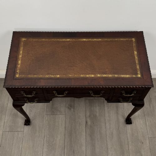 fig 8. An Edwardian dark mahogany writing table with five drawers, decorative brass handles, a carved top edge, and cabriole legs ending in ball and claw feet.