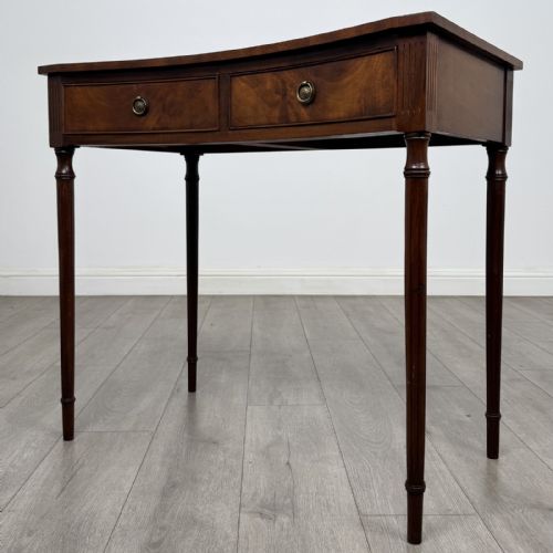 fig 1. An antique mahogany writing table with a concave bowfront shape, two drawers, brass ring handles, and four reeded legs.