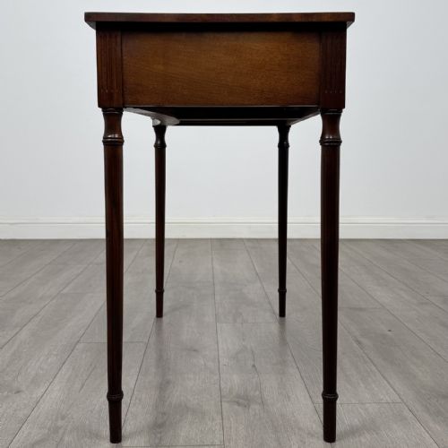 fig 2. An antique mahogany writing table with a concave bowfront shape, two drawers, brass ring handles, and four reeded legs.