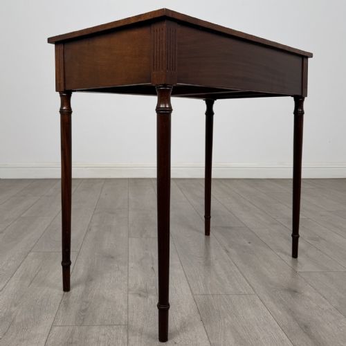 fig 3. An antique mahogany writing table with a concave bowfront shape, two drawers, brass ring handles, and four reeded legs.