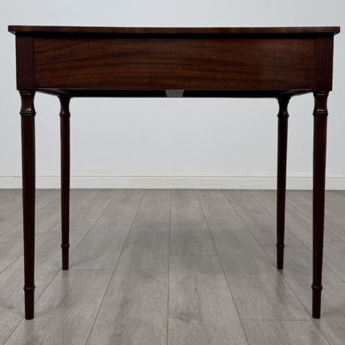 fig 4. An antique mahogany writing table with a concave bowfront shape, two drawers, brass ring handles, and four reeded legs.