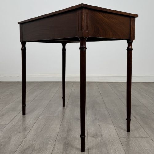 fig 5. An antique mahogany writing table with a concave bowfront shape, two drawers, brass ring handles, and four reeded legs.