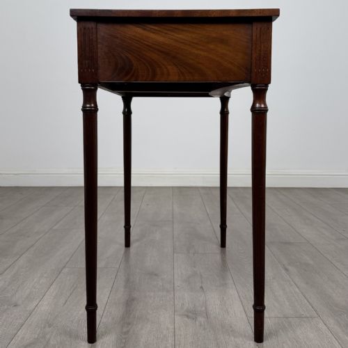 fig 6. An antique mahogany writing table with a concave bowfront shape, two drawers, brass ring handles, and four reeded legs.