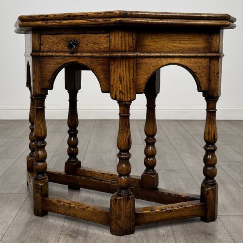 fig 1. An early 20th-century golden oak fold-over tea table featuring an octagonal top, arched frieze with a single central drawer, turned legs, and lower stretchers.