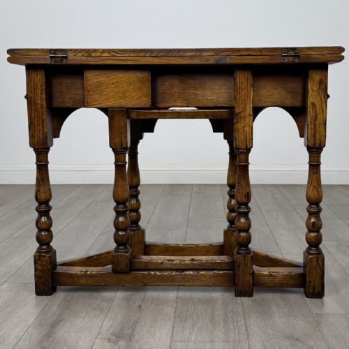 fig 4. An early 20th-century golden oak fold-over tea table featuring an octagonal top, arched frieze with a single central drawer, turned legs, and lower stretchers.