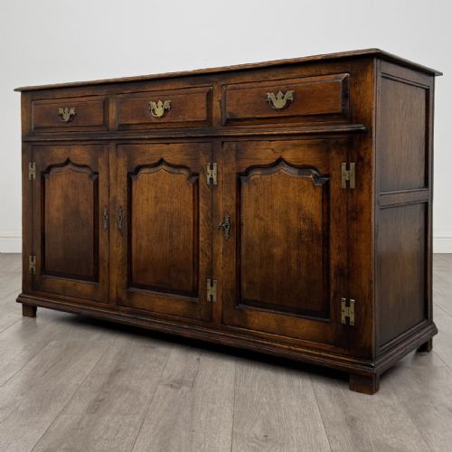 fig 1. A dark oak sideboard featuring three top drawers with brass handles above three fielded panel cabinet doors with exposed brass H-hinges.