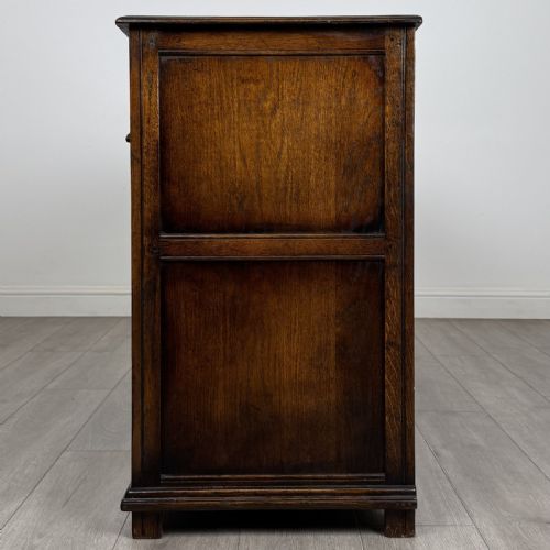 fig 2. A dark oak sideboard featuring three top drawers with brass handles above three fielded panel cabinet doors with exposed brass H-hinges.