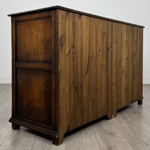 fig 3. A dark oak sideboard featuring three top drawers with brass handles above three fielded panel cabinet doors with exposed brass H-hinges.