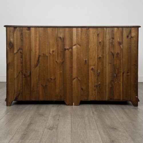 fig 4. A dark oak sideboard featuring three top drawers with brass handles above three fielded panel cabinet doors with exposed brass H-hinges.