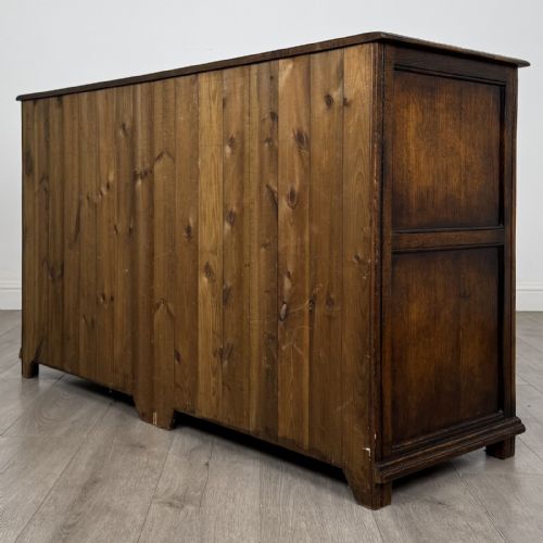 fig 5. A dark oak sideboard featuring three top drawers with brass handles above three fielded panel cabinet doors with exposed brass H-hinges.
