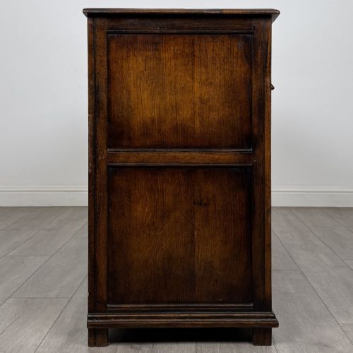 fig 6. A dark oak sideboard featuring three top drawers with brass handles above three fielded panel cabinet doors with exposed brass H-hinges.