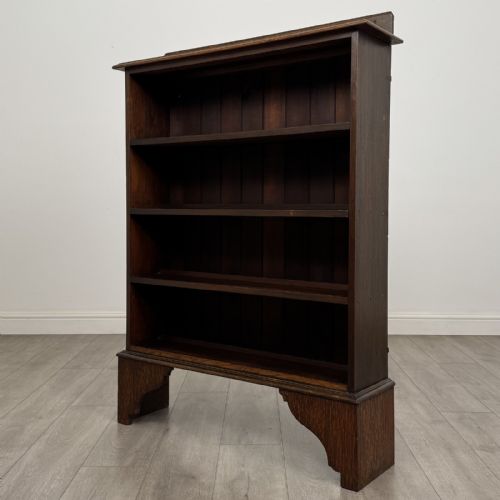 fig 1. An antique dark oak open bookcase featuring four horizontal shelves, a low raised top gallery, and shaped bracket feet.