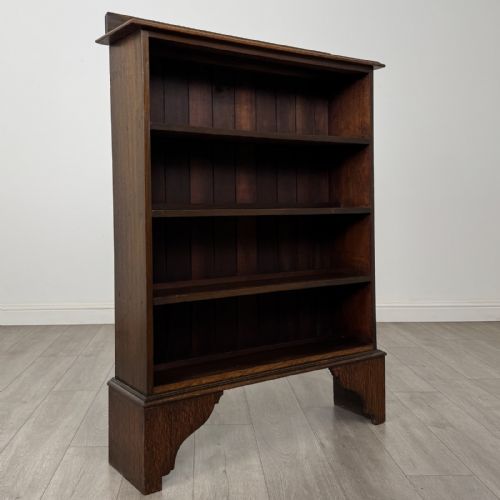 fig 7. An antique dark oak open bookcase featuring four horizontal shelves, a low raised top gallery, and shaped bracket feet.