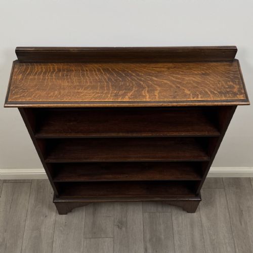 fig 8. An antique dark oak open bookcase featuring four horizontal shelves, a low raised top gallery, and shaped bracket feet.