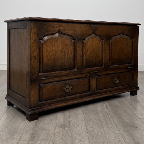 fig 7. A dark oak Georgian style drop-front mule chest featuring three arched fielded panels and two lower drawers with brass swan-neck handles.