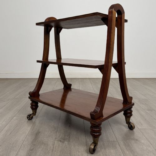 fig 4. A three-tier antique mahogany open bookcase featuring arched reeded uprights, turned legs, and brass castors.