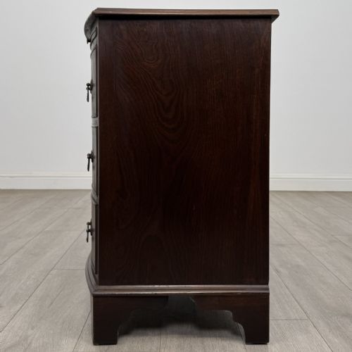 fig 2. A small dark mahogany bow-front chest of drawers featuring three drawers, a top pull-out slide, and brass swan-neck handles set on bracket feet.