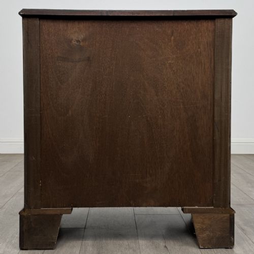 fig 4. A small dark mahogany bow-front chest of drawers featuring three drawers, a top pull-out slide, and brass swan-neck handles set on bracket feet.