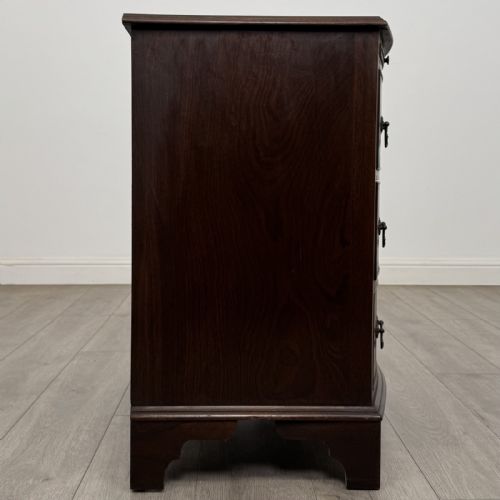 fig 6. A small dark mahogany bow-front chest of drawers featuring three drawers, a top pull-out slide, and brass swan-neck handles set on bracket feet.