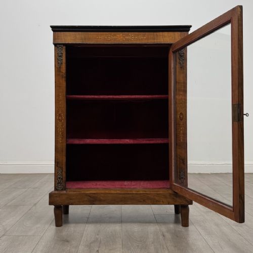 fig 1. A 19th-century Victorian walnut pier cabinet featuring floral marquetry inlays, decorative gilt metal mounts, a single glazed glass door, and velvet-lined interior shelves.
