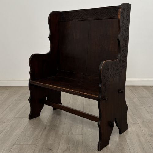 fig 1. A dark carved oak high-back settle featuring a floral carved frieze across the top and shaped side armrests.