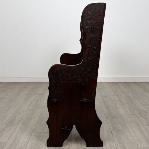 fig 2. A dark carved oak high-back settle featuring a floral carved frieze across the top and shaped side armrests.