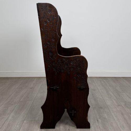 fig 6. A dark carved oak high-back settle featuring a floral carved frieze across the top and shaped side armrests.