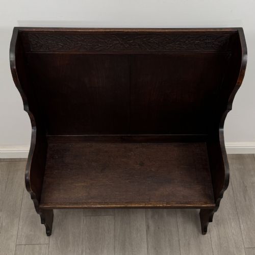 fig 8. A dark carved oak high-back settle featuring a floral carved frieze across the top and shaped side armrests.