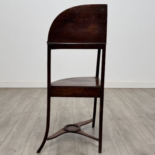 fig 2. A Georgian style mahogany corner washstand with a high curved splashback gallery, central drawer tier with brass rosette handles, and splayed legs joined by a circular lower stretcher.
