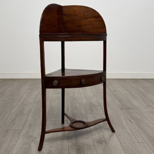 fig 5. A Georgian style mahogany corner washstand with a high curved splashback gallery, central drawer tier with brass rosette handles, and splayed legs joined by a circular lower stretcher.