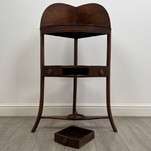 fig 7. A Georgian style mahogany corner washstand with a high curved splashback gallery, central drawer tier with brass rosette handles, and splayed legs joined by a circular lower stretcher.